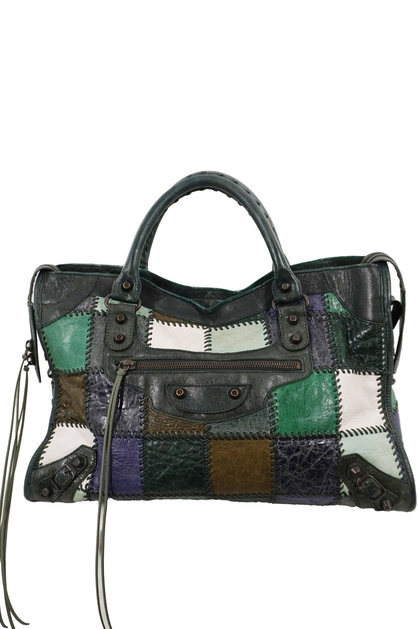 Balenciaga patchwork city bag featuring leather panels in green, purple, brown, and white, combined with smooth black leather. The bag has dual top handles, a front flap pocket with metal studs, and long leather tassels hanging from the sides, shown against a plain white background.
