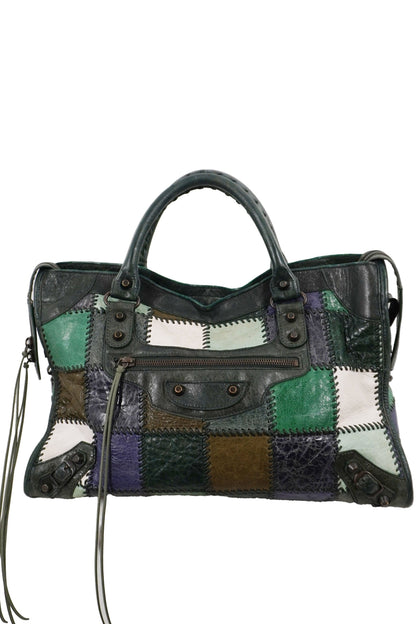 Balenciaga patchwork city bag featuring leather panels in green, purple, brown, and white, combined with smooth black leather. The bag has dual top handles, a front flap pocket with metal studs, and long leather tassels hanging from the sides, shown against a plain white background.